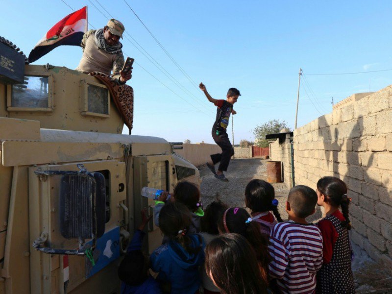 Des enfants jouent près d'un blindé des forces irakiennes patrouillant dans une rue du village de Jarif, à environ 45 kilomètres au sud de Mossoul, le 12 novembre 2016 - SAFIN HAMED [AFP]