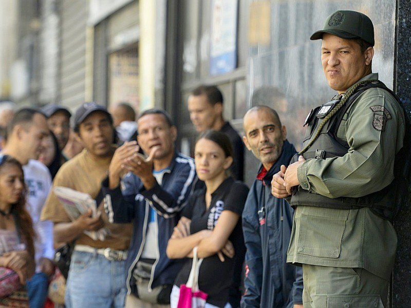 Un militaire vénézuélien surveille ceux qui font la queue devant la banque centrale de Caracas pour échanger leurs billets de 100 bolivars, le 16 décembre 2016 - FEDERICO PARRA [AFP]