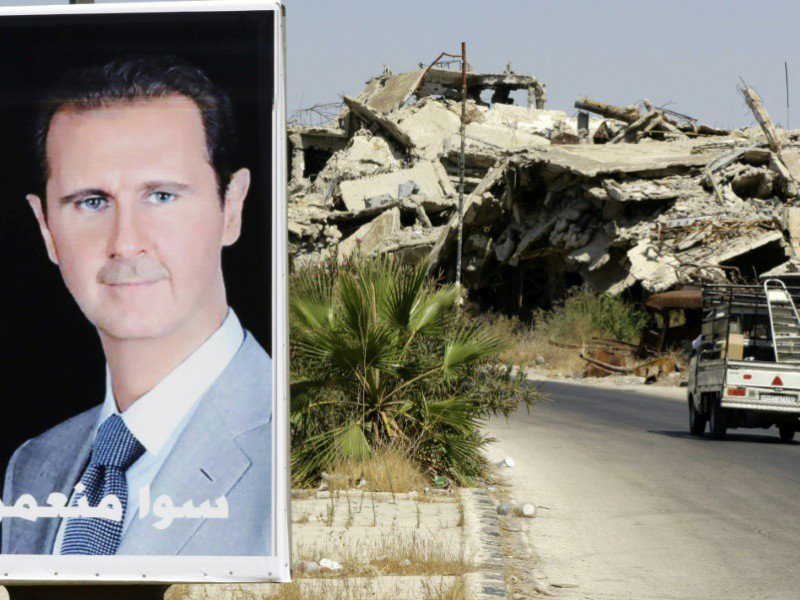 Un véhicule passe à côté d'une affiche de Bachar al-Assad et des bâtiment détruits du quartier Jouret al-Shiah à Homs le 19 septembre 2016 - LOUAI BESHARA [AFP/Archives]