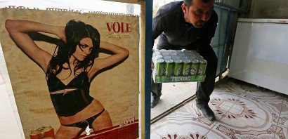 Un homme, qui apporte des canettes de bière dans la boutique de Wissam Ghanem, passe à côté d'un poster de femme en sous-vêtements, le 17 février 2017 à Bachiqa, près de Mossoul, en Irak - STRINGER [AFP]