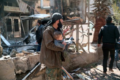 Un homme porte un enfant dans ses bras après une frappe aérienne sur Hamouria près de Damas au cours de laquelle au moins 16 civils sont morts et des dizaines de personnes ont été blessées, le 25 mars 2017 - Msallam ABDALBASET [AFP]