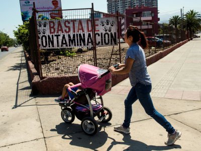 Une femme et son enfant dans une poussette passent devant un panneau dénonçant la pollution, le 9 mars 2017 à Antofagasta, au Chili - Martin BERNETTI [AFP]