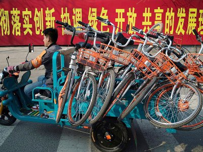 Un homme conduit un véhicule rempli de vélos partagés qui vont être installés près d'une station de métro à Pékin le 28 mars 2017 - Nicolas ASFOURI [AFP]