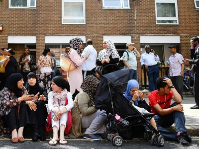 Des personnes affectées par le feu qui a ravagé la Tour Grenfell, assises sur le trottoir à l'extérieur d'un centre d'aide temporaire dans l'ouest de Londres le 14 juin 2017 - Ben STANSALL [AFP]