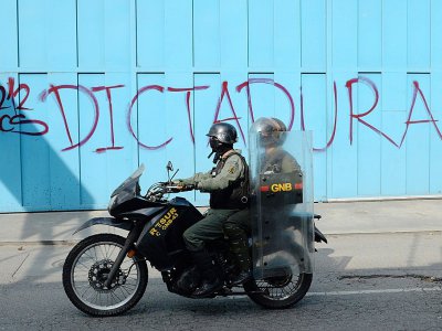 Les policiers de la Garde nationale passent devant un graffiti disant que le Venezuela bascule sous une dictature, le 6 juillet 2017 à Caracas - Federico Parra [AFP]