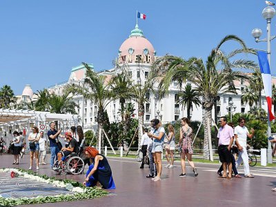 Des passants se recueillent sur la Promenade des Anglais, près des fleurs déposées en hommage aux victimes de l'attentat de Nice, le 14 juillet 2017, un an après l'attaque - YANN COATSALIOU [AFP]