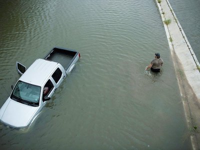 Un américain passe devant une voiture abandonnée alors que les eaux continuent de monter à Houston, le 28 août 2017 - Brendan Smialowski [AFP]