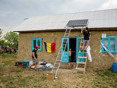 Iulian Angheluta (g) et un bénévole installent un panneau solaire sur le toit d'une maison, le 25 juillet 2017 à Gorbanesti, en Roumanie - ANDREI PUNGOVSCHI [AFP]