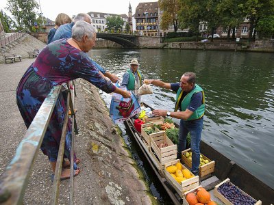 Christophe Moegling (G), et l'un de ses employés vendent des fruits et des légumes depuis la barque à fond plat faisant office de marché flottant sur la rivière de l'Ill à Strasbourg (est), le 6 septembre 2017 - PATRICK HERTZOG [AFP]