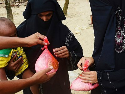 Un homme distribue de l'aide alimentaire à une femme Rohingya à Teknaf au Bangladesh le 12 septembre 2017 - MUNIR UZ ZAMAN [AFP]