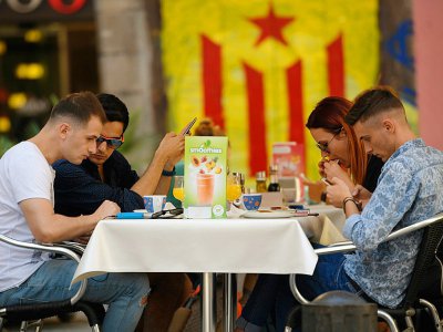 Un groupe de touristes assis devant un graffiti représentant le drapeau pro-indépendant de la Catalogne, le 13 septembre, à Barcelone. - LLUIS GENE [AFP]