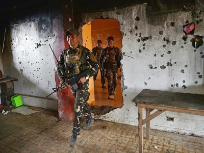 Des soldats gouvernementaux passent par une trouée dans un mur criblé de balles à l'intérieur d'une maison à Marawi le 25 octobre 2017 trois jours après la reprise de la ville aux jihadistes par l'armée philippine - TED ALJIBE [AFP]