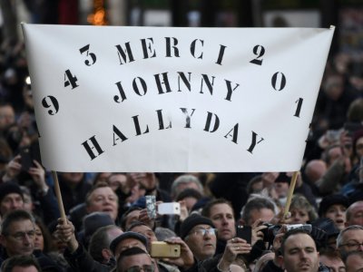 La foule brandit une pancarte "Merci Johnny Hallyday", le 9 décembre 2017 devant l'Eglise de la Madeleine à Paris - BERTRAND GUAY [AFP]
