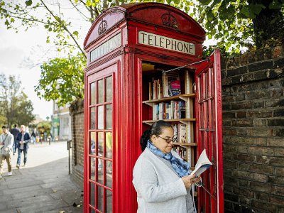 Patsy Ari feuillette un livre près d'une ancienne cabine téléphonique reconvertie en bibliothèque d'échange, à Londres, le 21 octobre 2017 - TOLGA AKMEN [AFP]