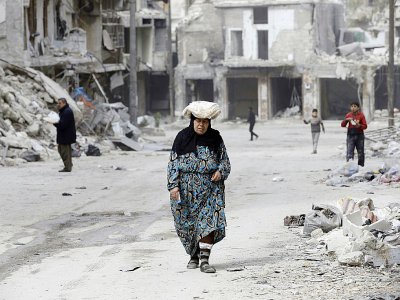 Une femme marche dans une rue encombrée de gravats dans l'ancien quartier rebelle d'Al-Chaar à Alep, le 9 mars 2017 - JOSEPH EID [AFP]