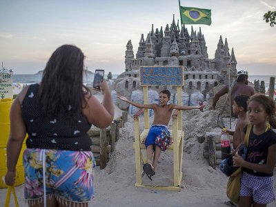 Des gens prennent des photos du château de sable de Marcio Mizael Matolias, le 18 janvier 2018 sur la plage de Barra da Tijuca, à Rio de Janeiro - MAURO PIMENTEL [AFP]