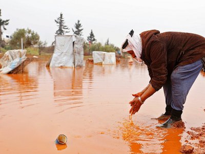 Abou Khaled se lave les mains dans une flaque d'eau boueuse formée par les fortes pluie dans un camp de fortune de déplacés à Batabou, à la frontière entre les provinces syriennes d'Idleb et d'Alep, le 24 janvier 2018 - OMAR HAJ KADOUR [AFP]