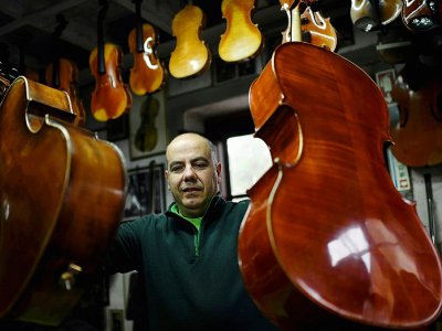 Joaquim Capela porte deux violoncelles, dans l'atelier familial de lutherie, le 15 février 2018 - FRANCISCO LEONG [AFP]