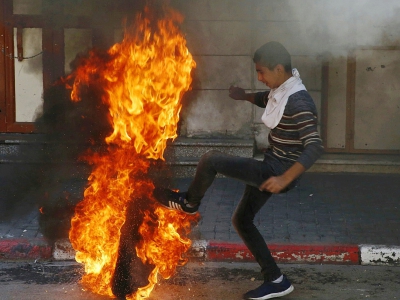 Un manifestant palestinien donne un coup de pied dans un pneu en feu vers des soldats israéliens, le 31 mars 2018 à Hébron, en Cisjordanie - HAZEM BADER [AFP]