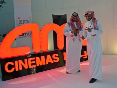 Des Saoudiens posent devant le logo du géant américain AMC Entertainment, première société autorisée à exploiter des cinélas eb Arabie saoudite, le 18 avril 2018 à Ryad - Fayez Nureldine [AFP]