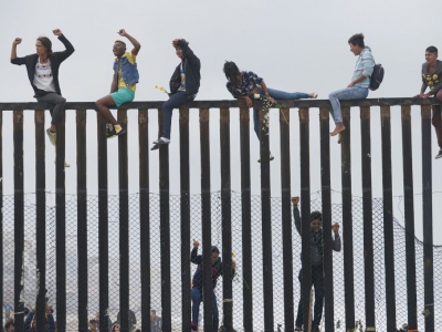 Des demandeurs d'asile Centre-américains "à califourchon" sur la frontière séparant le Mexique des États-Unis, le 29 avril 2018 à Tijuana (Mexique) - Sandy Huffaker [AFP]