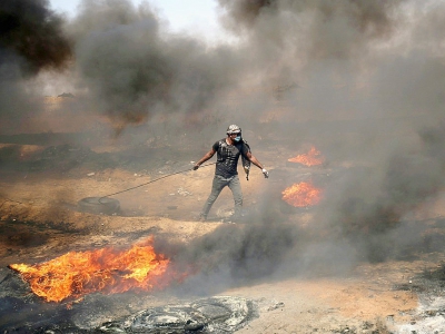 Un manifestant palestinien tire un pneu en feu durant les heurs frontaliers avec l'armée israélienne, le 11 mai 2018 dans la bande de Gaza - SAID KHATIB [AFP/Archives]