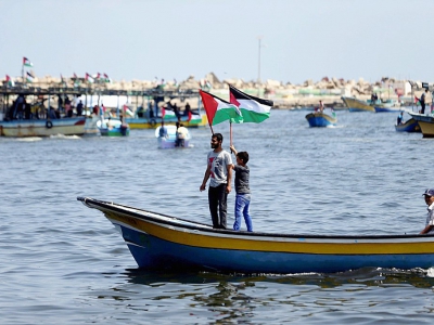 Des Palestiniens agitent leur drapeau sur un bateau de pêche tandis qu'ils prennent la mer le 29 mai 2018 depuis le port de Gaza - MAHMUD HAMS [AFP]