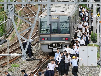 Des passagers d'un train marchent sur les rails après une interruption du trafic ferroviaire due à un fort séisme à Osaka au Japon, le 18 juin 2018 - STR [JIJI PRESS/AFP]
