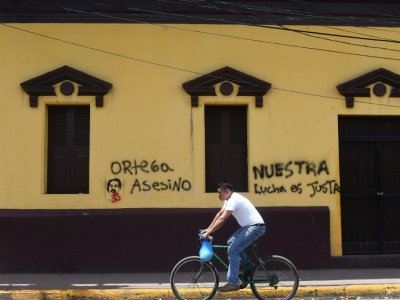 Un homme passe à bicyclette devant des inscriptions "Ortega assassin" et "Notre lutte est juste", dans la ville de Masaya, le 20 juin 2018 - MARVIN RECINOS [AFP]