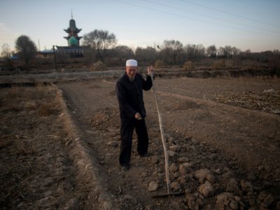 Un Chinois musulman travaille dans son champ, une mosquée en arrière-plan, le 2 mars 2018 près de Linxia, dans le nord-ouest de la Chine - Johannes EISELE [AFP]