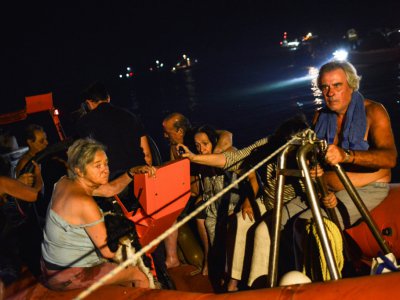 Des secouristes et des bénévoles aident à évacuer les habitants de Mati qui ont pu échapper à l'incendie en gagnant la mer, dans la nuit du 23 au 24 juillet 2018 - ANGELOS TZORTZINIS [AFP]