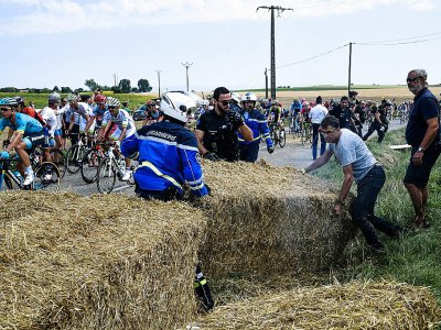 Des gendarmes libèrent la chaussée brièvement bloquée par les agriculteurs à coup de meules de foin durant la 14e étape du Tour, le 24 juillet 2018 - Jeff PACHOUD [AFP]