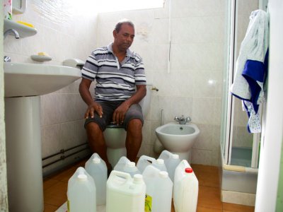 Un habitant pose avec ses bidons utilisés pour stocker l'eau dans sa salle de bain à Capesterre, en Guadeloupe, le 26 juillet 2018 - Cedrick Isham CALVADOS [AFP]