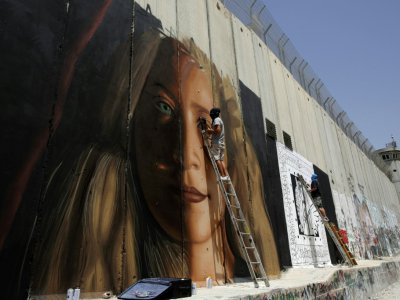 L'artiste de rue italien Jorit Agoch peint un portrait géant d'Ahed Tamimi, une adolescente palestinienne emprisonnée depuis huit mois, sur le mur construit par Israël en Cisjordanie occupée. Photo prise à Bethléem, le 25 juillet 2018 - Musa Al SHAER [AFP]