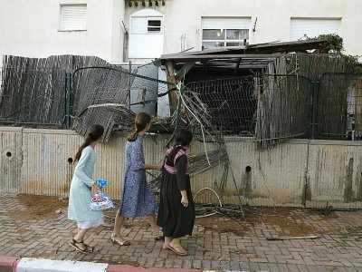 Des habitants de la ville de Sdérot dans le sud d'Israël passent devant une clôture endommagée par la chute d'une roquette tirée de la bande de Gaza, le 14 juillet 2018 - Ahmad GHARABLI [AFP]