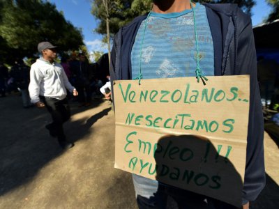 Un homme porte une pancarte sur laquelle il est écrit "Vénézuéliens à la recherche d'un emploi", dans un campement de fortune près d'une gare de bus, le 9 août 2018 à Quito, en Equateur - RODRIGO BUENDIA [AFP]