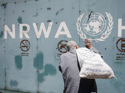 Un Palestinien devant l'emblème de l'Unrwa, l'agence de l'ONU pour les réfugiés palestiniens, devant ses bureaux de la ville de Gaza, le 31 juillet 2018 - SAID KHATIB [AFP]