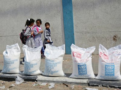 Des écolières palestiniennes passent devant des sacs de farine entreposés à l'extérieur des bureaux de l'agence onusienne pour les réfugiés palestiniens (Unrwa) dans le camp de Rafah, dans le sud de la bande de Gaza, le 1er septembre 2018 - SAID KHATIB [AFP]