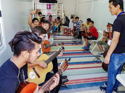 Des réfugiés et des migrants suivent un cours de guitare dans le camps de Moria, sur l'île de Lesbos, le 25 septembre 2018 - Aris MESSINIS [AFP]