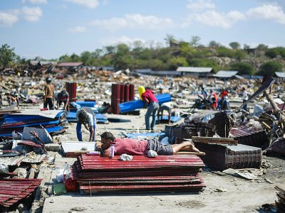 Un homme s'est allongé sur des tôles empilées au milieu des décombres, le 1er octobre 2018 à Palu dans l'île des Célèbes en Indonésie, tandis que d'autres cherchent à récupérer des objets quatre jours après un séisme meurtrier - Jewel SAMAD [AFP]