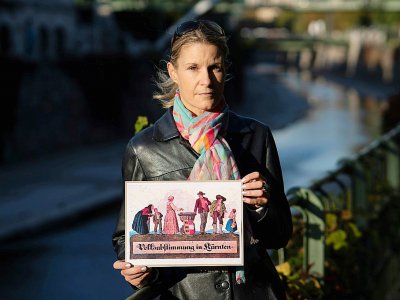 Carmen Kuster pose, le 5 octobre 2018 à Vienne, avec une gravure présentant une famille déposant un bulletin dans l'urne sur laquelle repose un blason aux couleurs de la Carinthie. Avec l'éclatement de l'empire des Habsbourg, les électeurs ont dû cho - JOE KLAMAR [AFP]