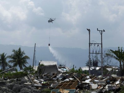 Photographie prise le 18 octobre 2018, à Palu en Indonésie, montrant un hélicoptère pulvériser du désinfectant au dessus de la zone dévastée par un tsunami le 28 septembre - YUSUF WAHIL [AFP/Archives]