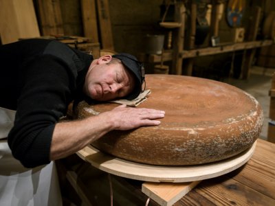 Le fromager Beat Wampfler pose sa tête sur une meule d'emmental dont l'affinage se déroule en musique, le 19 octobre 2018 à Berthoud, en Suisse - Fabrice COFFRINI [AFP]