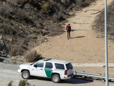 Un homme avec un enfant dans les bras chemine vers une patrouille américaine après avoir traversé illégalement la frontière, depuis la ville mexicaine de Tijuana, le 13 novembre 2018 - Guillermo Arias [AFP]