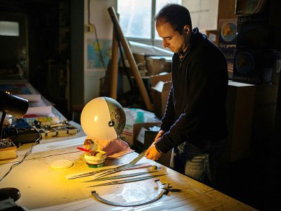 Michael Koimitzis découpe des bandes de carte qu'il collera sur une sphère pour fabriquer un globe terrestre, dans son atelier d'Athènes le 5 novembre 2018 - ANGELOS TZORTZINIS [AFP]