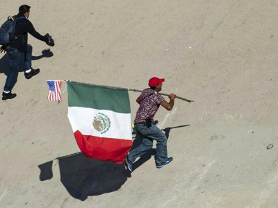 Un migrant portant les drapeaux mexicain et étatsunien tente de passer la frontière entre le Mexique et les Etats-Unis le 25 novembre 2018 à Tijuana - Pedro PARDO [AFP]