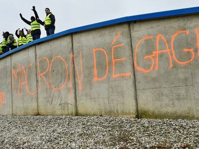 Manifestants en gilets jaunes à un rond-point au-dessus d'un tag "Macron dégage", à Saint-Saturnin près du Mans le 24 novembre 2018 - Jean-François MONIER [AFP/Archives]