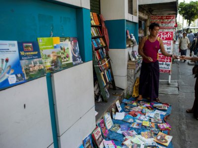 Le bouquiniste Tin Than (à gauche) montre un livre à un client devant son étal installé à même la rue de Pansodan, dans la capitale birmane Rangoun, le 5 décembre 2018 - Ye Aung THU [AFP]
