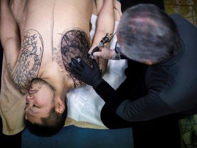 Le tatoueur japonais Horiyoshi III travaille sur un motif pour son client Kazuhide Okumura (à gauche), dans son studio de Yokohama, le 27 janvier 2018 - Behrouz MEHRI [AFP]