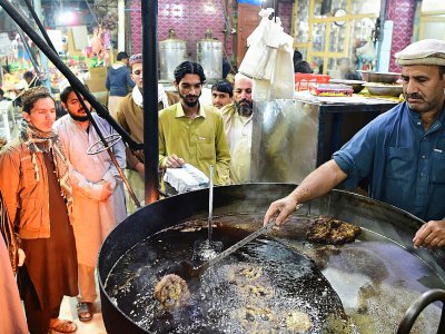 Un cuisinier fait griller des kebabs sous l'oeil de ses clients dans le quartier de Namak Mandi à Peshawar, le 13 décembre 2018 - ABDUL MAJEED [AFP]